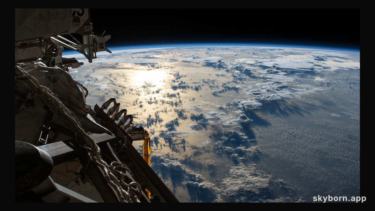 The Sun's glint reflects off the Pacific Ocean shadowed by a line of cumulonimbus clouds as the International Space