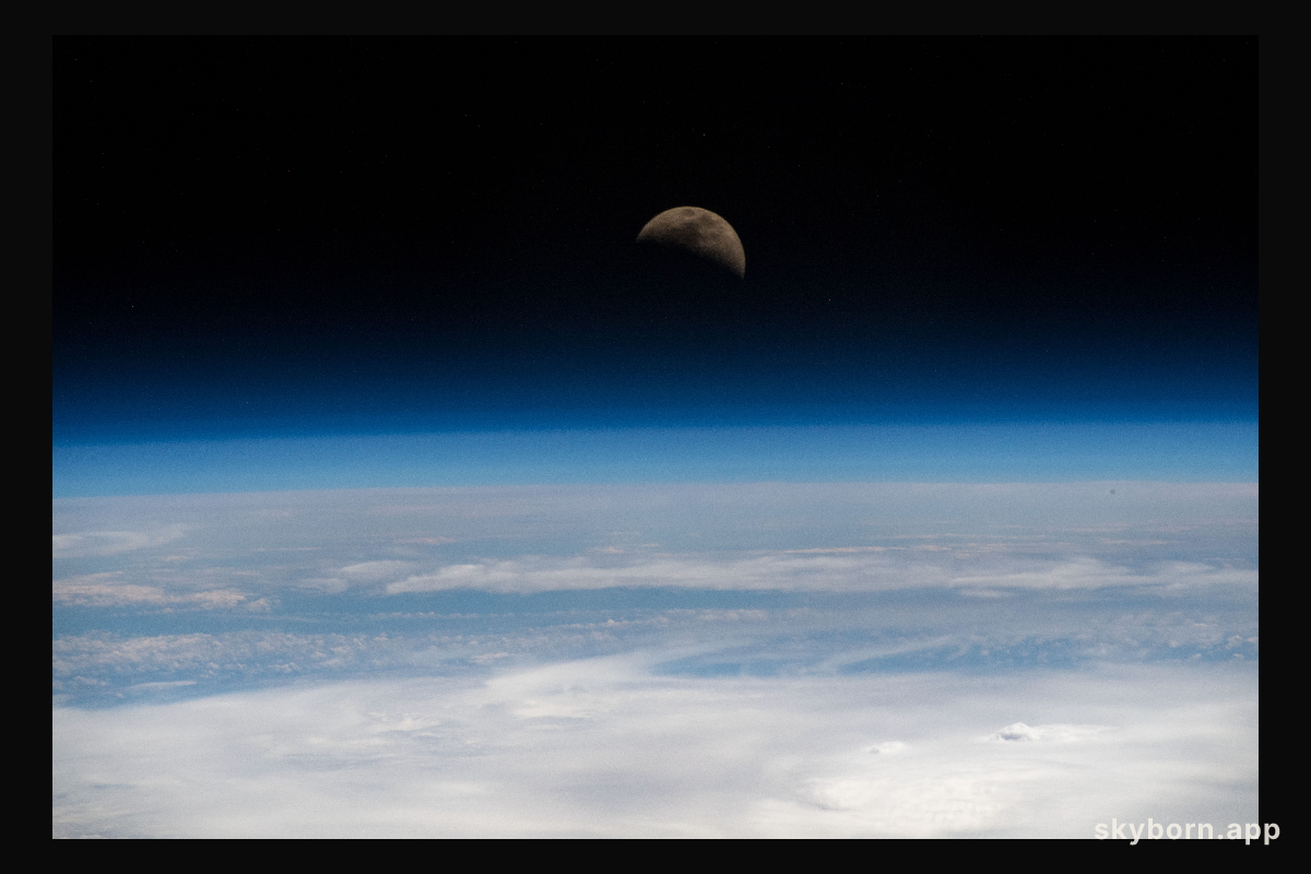 The moon is photographed in its first quarter phase just above the Earth's limb as the International Space Station