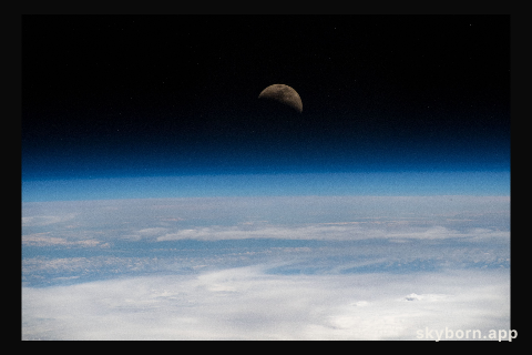 The moon is photographed in its first quarter phase just above the Earth's limb as the International Space Station