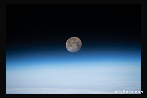 The moon is photographed in its waning gibbous phase just above the Earth's limb as the International Space Station