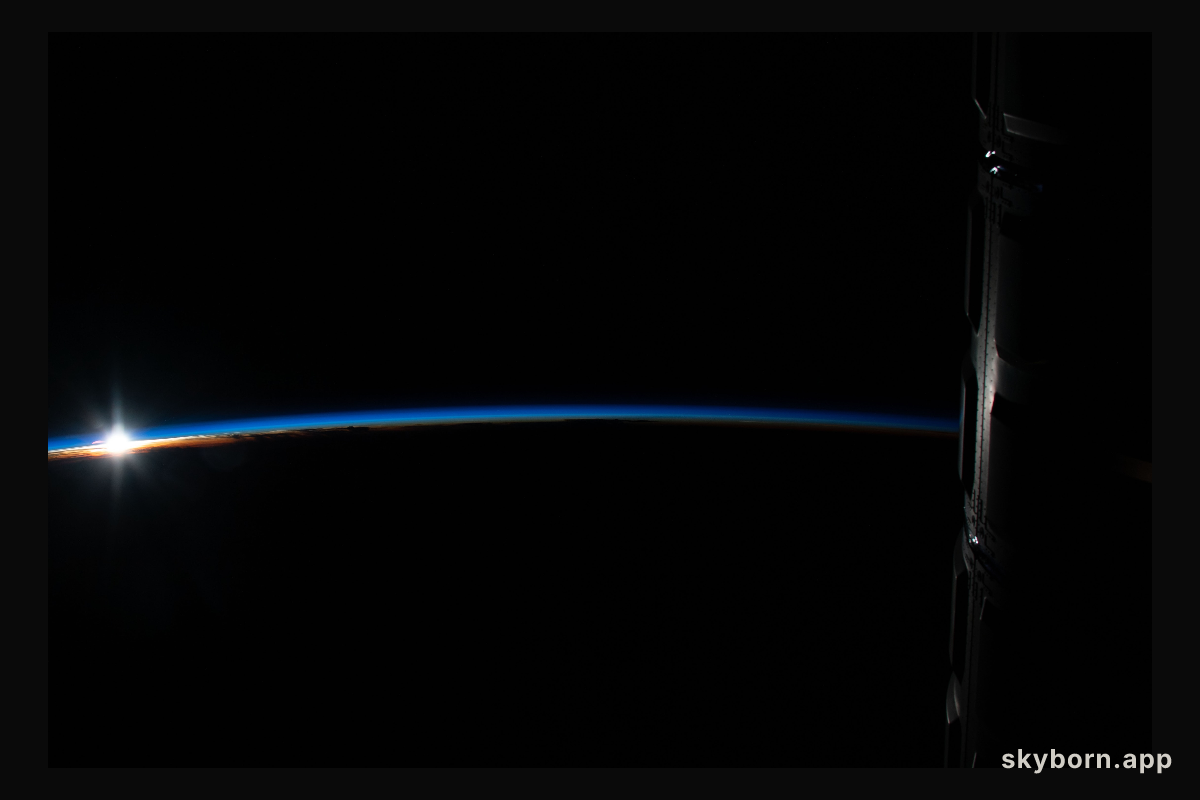 The sun's first rays peek above Earth's limb highlighting the thin blue atmosphere during an orbital sunrise