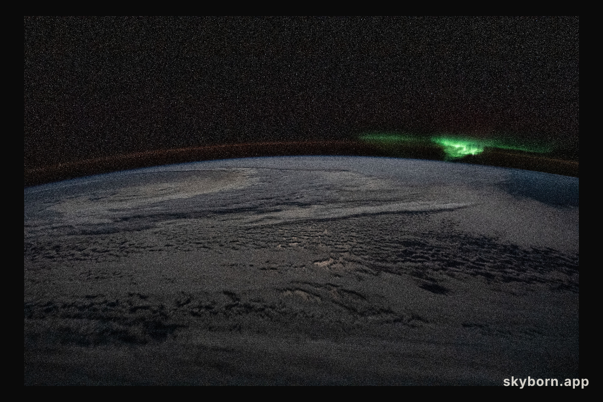 The atmospheric glow and a wispy aurora australis, also known as the "southern lights," frame a cloud-covered Earth