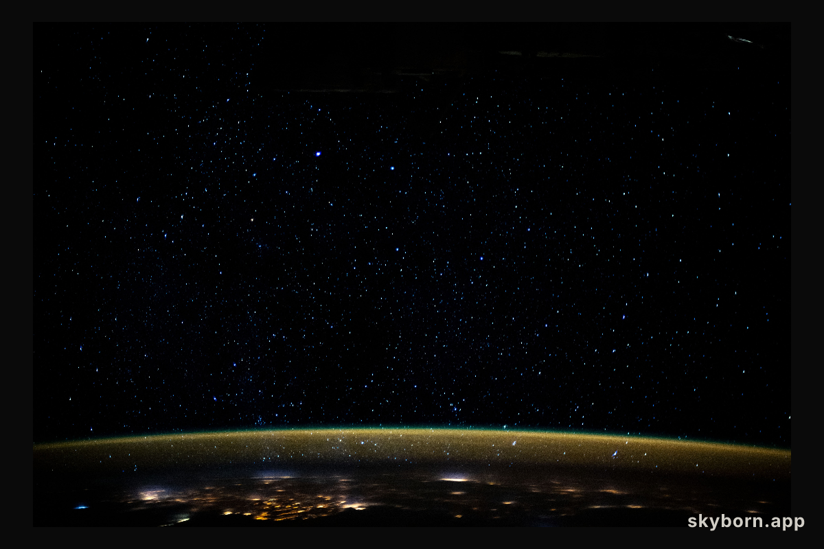 Stars glitter in the night sky above an atmospheric glow that blankets the city lights as the International Space