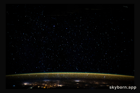 Stars glitter in the night sky above an atmospheric glow that blankets the city lights as the International Space