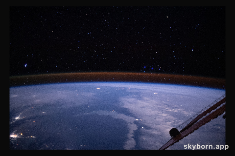 The amber hue hovering just above the Earth's limb is the atmospheric glow with the Milky Way's stars sparkling