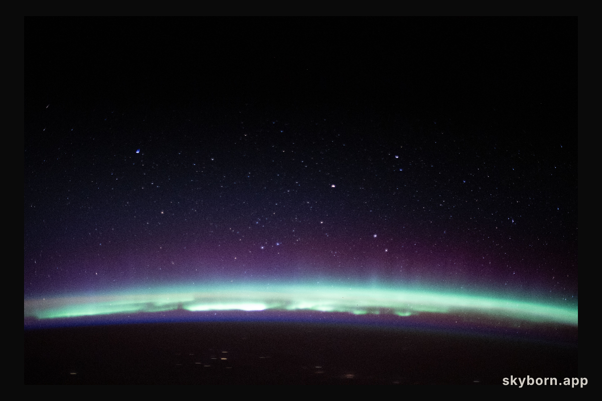 A radiant aurora crowns the Earth's horizon beneath a starry sky as the International Space Station orbited 262 miles