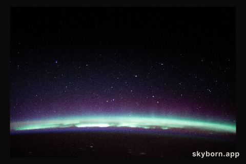 A radiant aurora crowns the Earth's horizon beneath a starry sky as the International Space Station orbited 262 miles