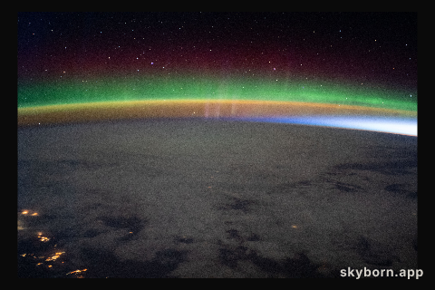 A bright aurora crowns Earth's horizon beneath a starry sky as the International Space Station flew into an orbital