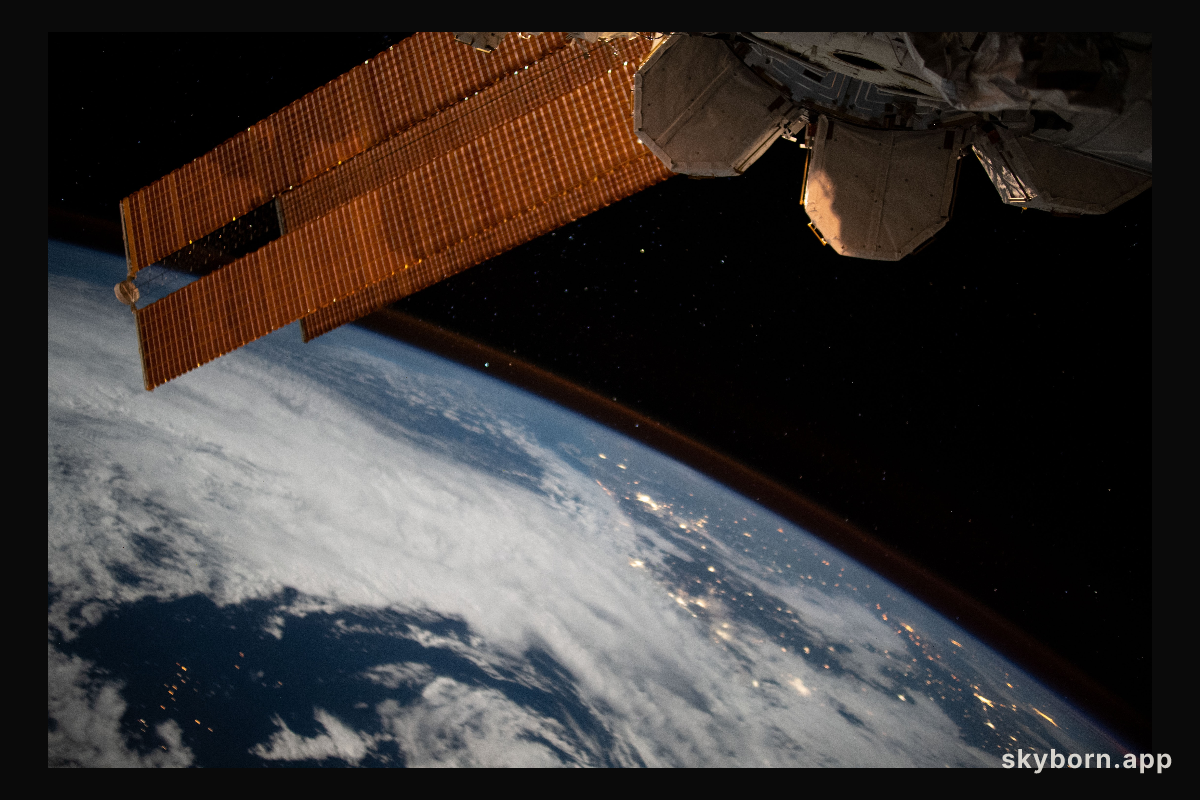 The city lights of Brazil sparkle underneath cloudy skies and a dim atmospheric glow as the International Space Station