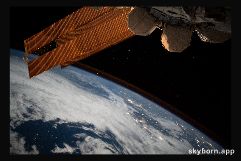 The city lights of Brazil sparkle underneath cloudy skies and a dim atmospheric glow as the International Space Station