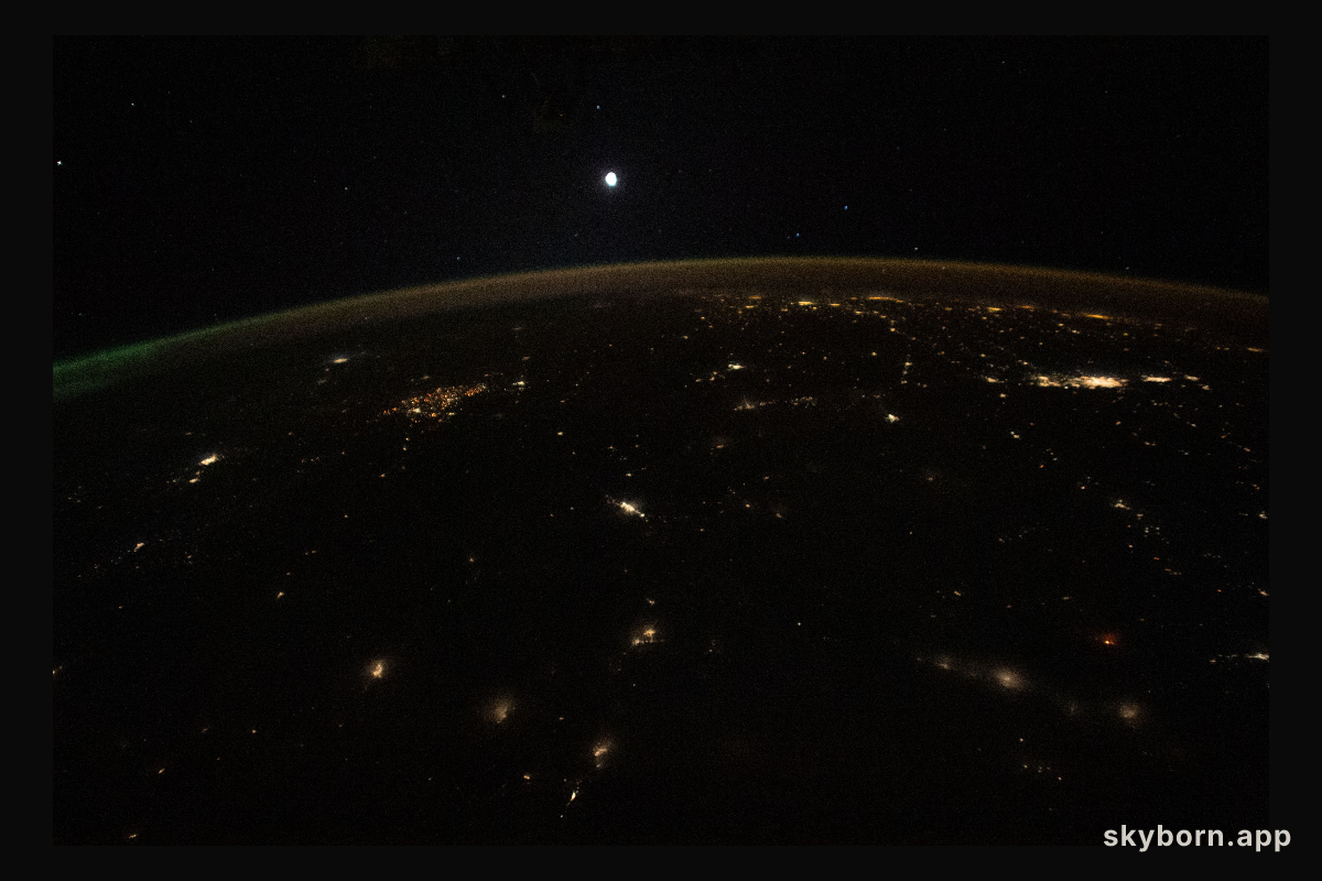 The Moon is pictured above Earth's horizon, its airglow, and an aurora (at far right) in this photograph