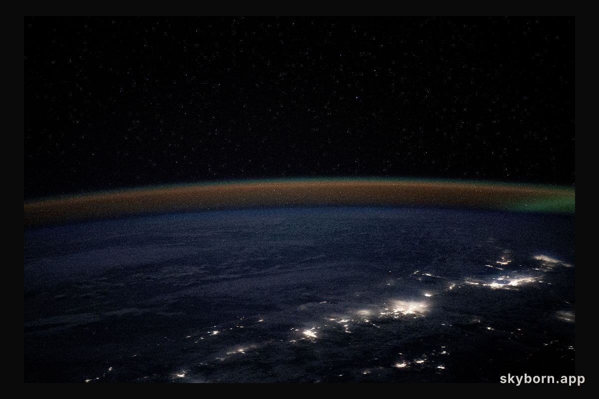 An atmospheric glow blankets Earth's horizon as city lights outline the northwestern coast of the United States