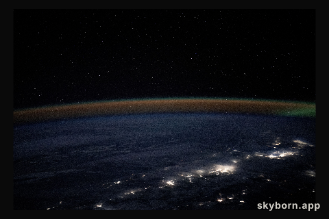 An atmospheric glow blankets Earth's horizon as city lights outline the northwestern coast of the United States
