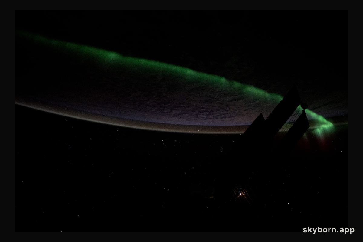 An atmospheric glow crowns Earth's horizon as an aurora streams