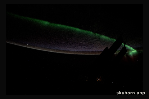 An atmospheric glow crowns Earth's horizon as an aurora streams