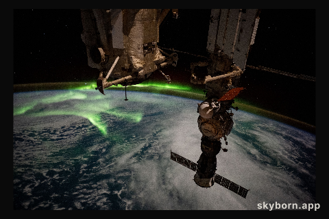 The aurora australis arcs back and forth above a partly cloudy Indian Ocean