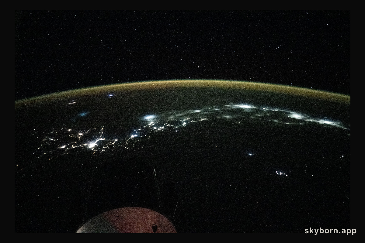 City lights trace the Japanese coastline underneath a dim yellow-green airglow
