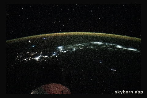 City lights trace the Japanese coastline underneath a dim yellow-green airglow