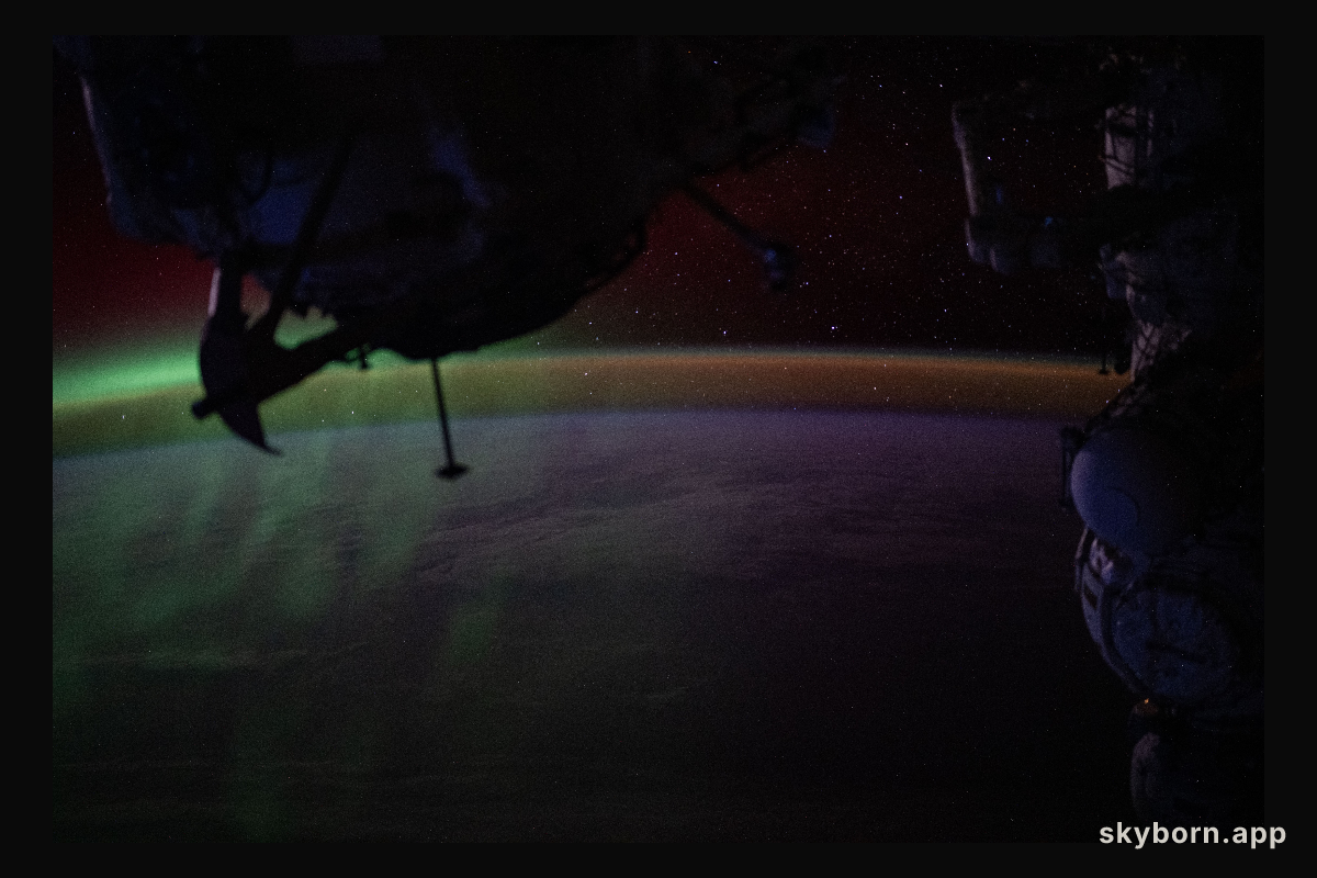 A wispy green aurora australis fades into a dim orange-yellow airglow above Earth’s horizon