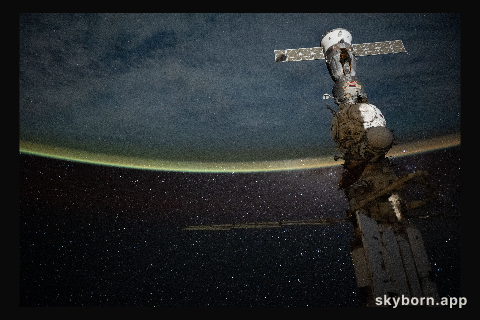 A yellow-green airglow blankets Earth’s horizon beneath a star-filled sky