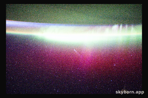 A bright, neon-like aurora radiates above Earth and seemingly absorbs Comet Lemmon