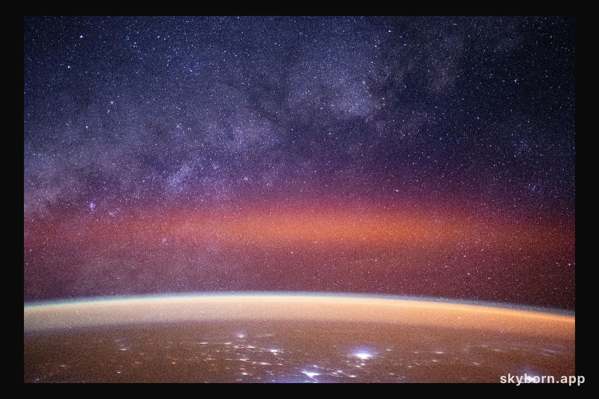 The Milky Way spans the night sky above a bright orange-yellow airglow
