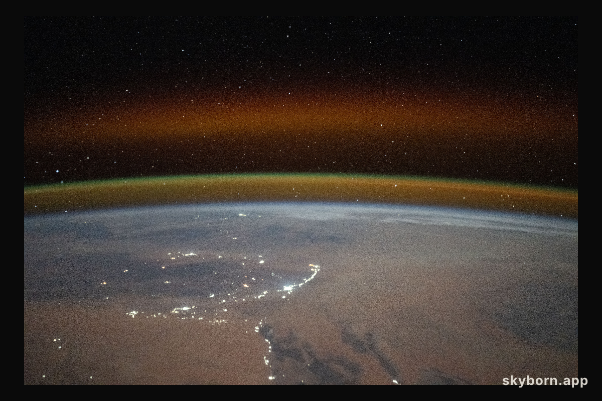 A yellow-red airglow blankets Earth's horizon above the Saharan landscape of Algeria