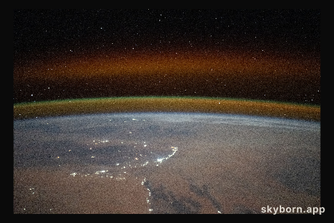 A yellow-red airglow blankets Earth's horizon above the Saharan landscape of Algeria