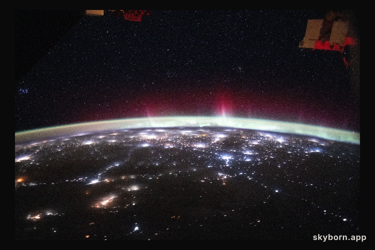 An aurora streams above Earth’s atmospheric glow