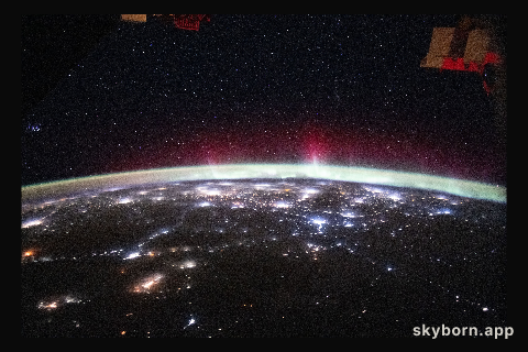 An aurora streams above Earth’s atmospheric glow