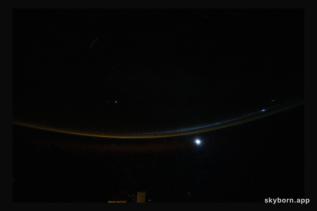 A dim airglow blankets Earth’s horizon as a faint Moon sets above the Indian Ocean